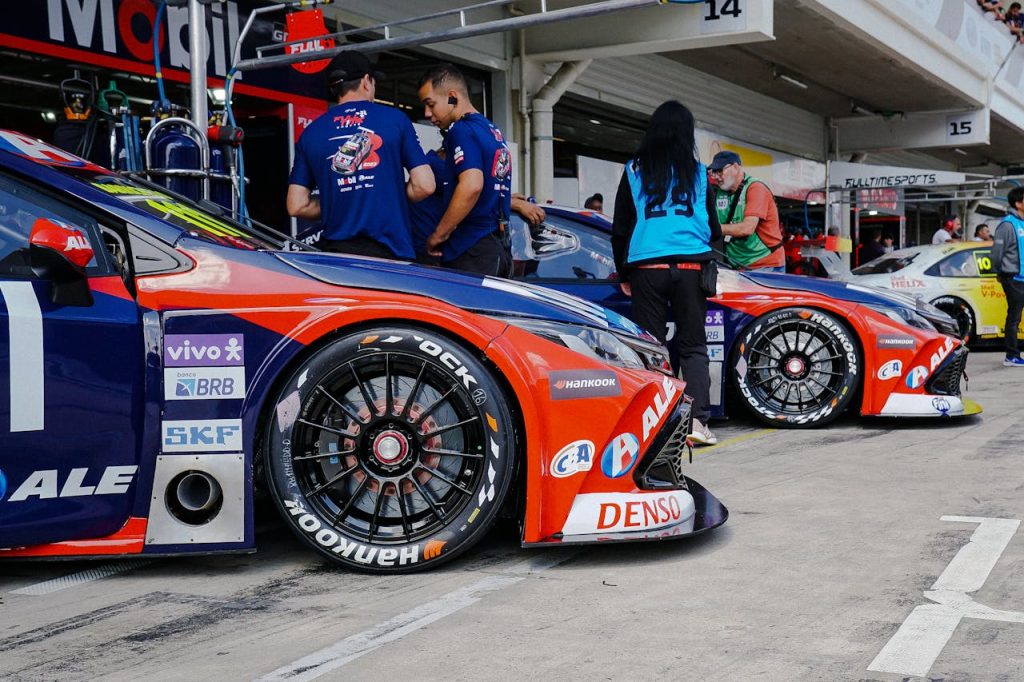 Close-up of colorful race cars in a pit stop with mechanics and crew preparing for a motorsport event.